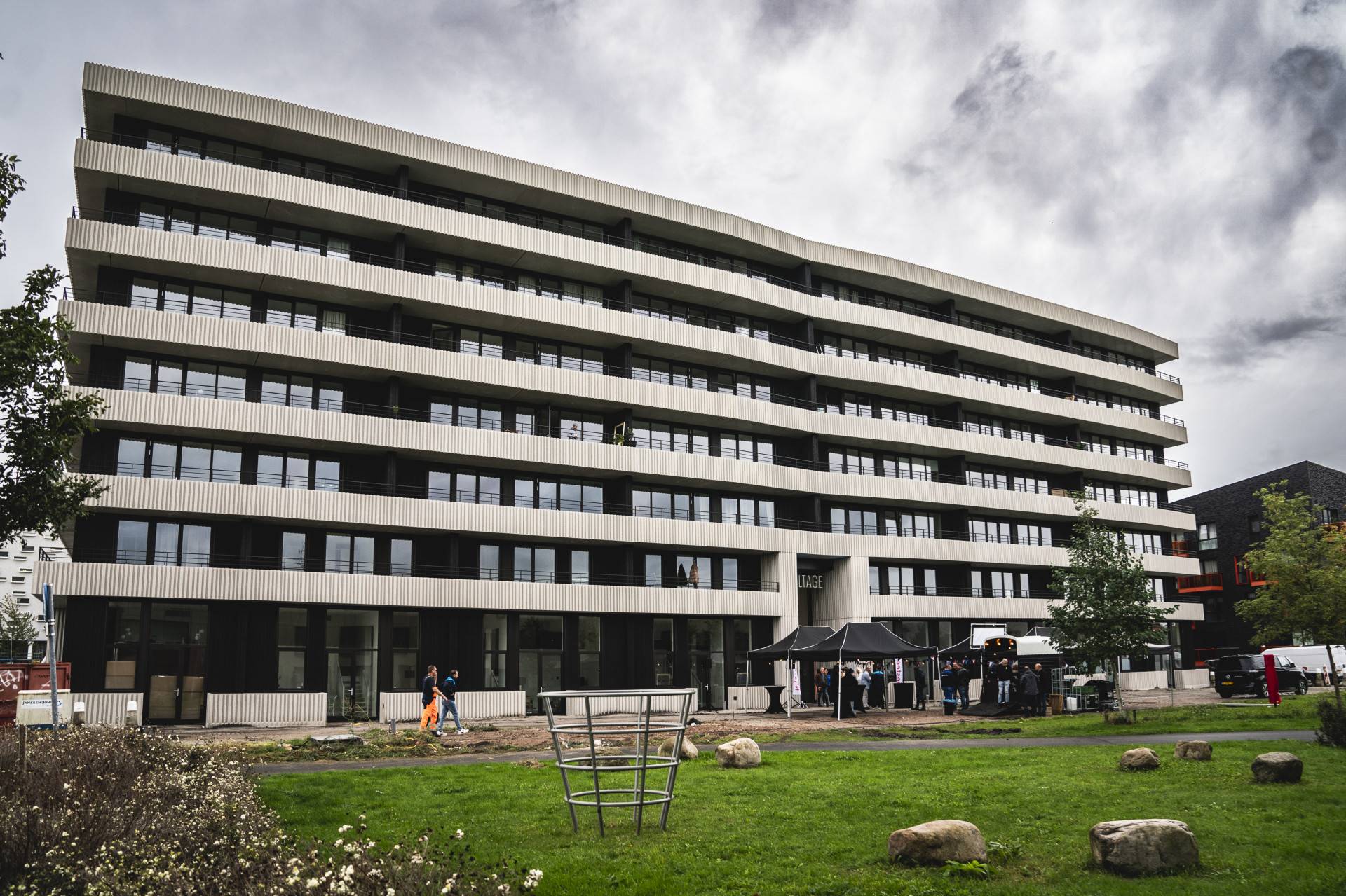 Modern appartementsgebouw met groene omgeving en bewolkte lucht.