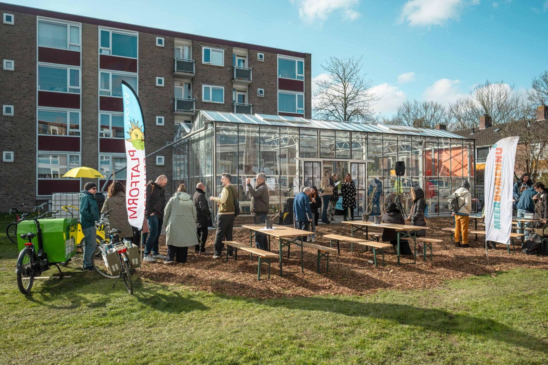 Een groep mensen verzameld voor een kas in een stadsomgeving.