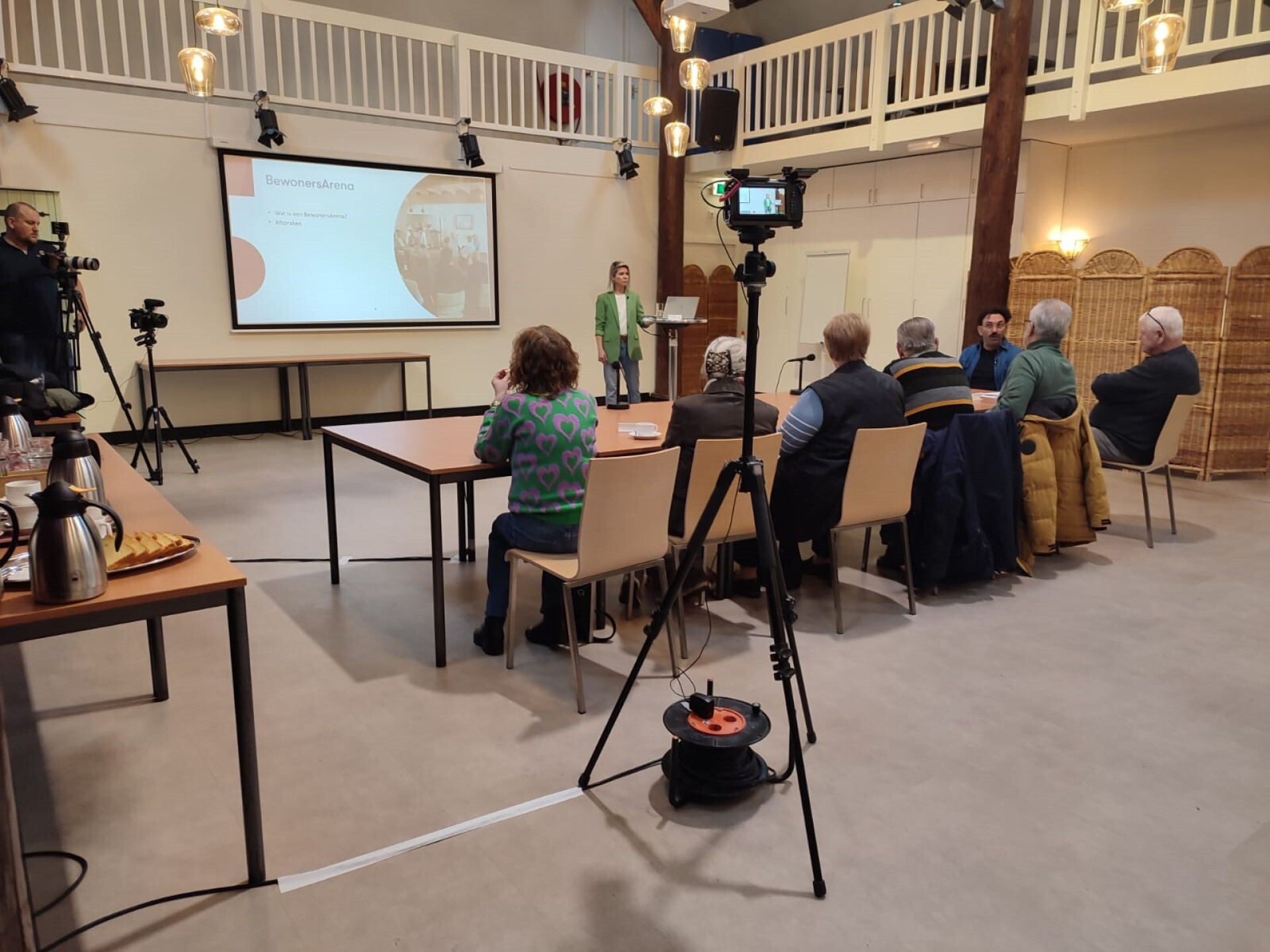 Mensen wonen een presentatie bij in een zaal met camera-opstellingen.