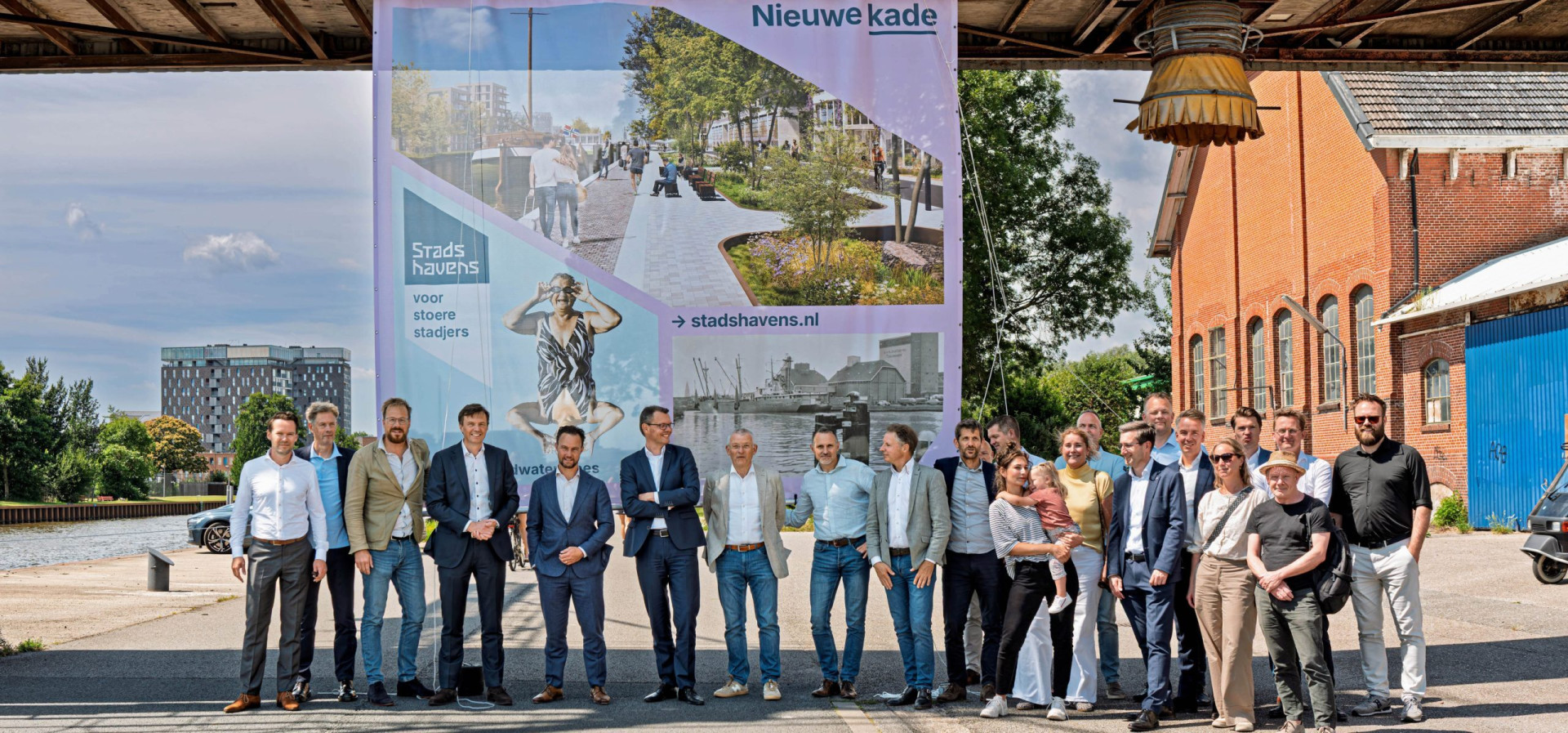 Groep mensen bij een bouwbord voor een stadsontwikkelingsproject.
