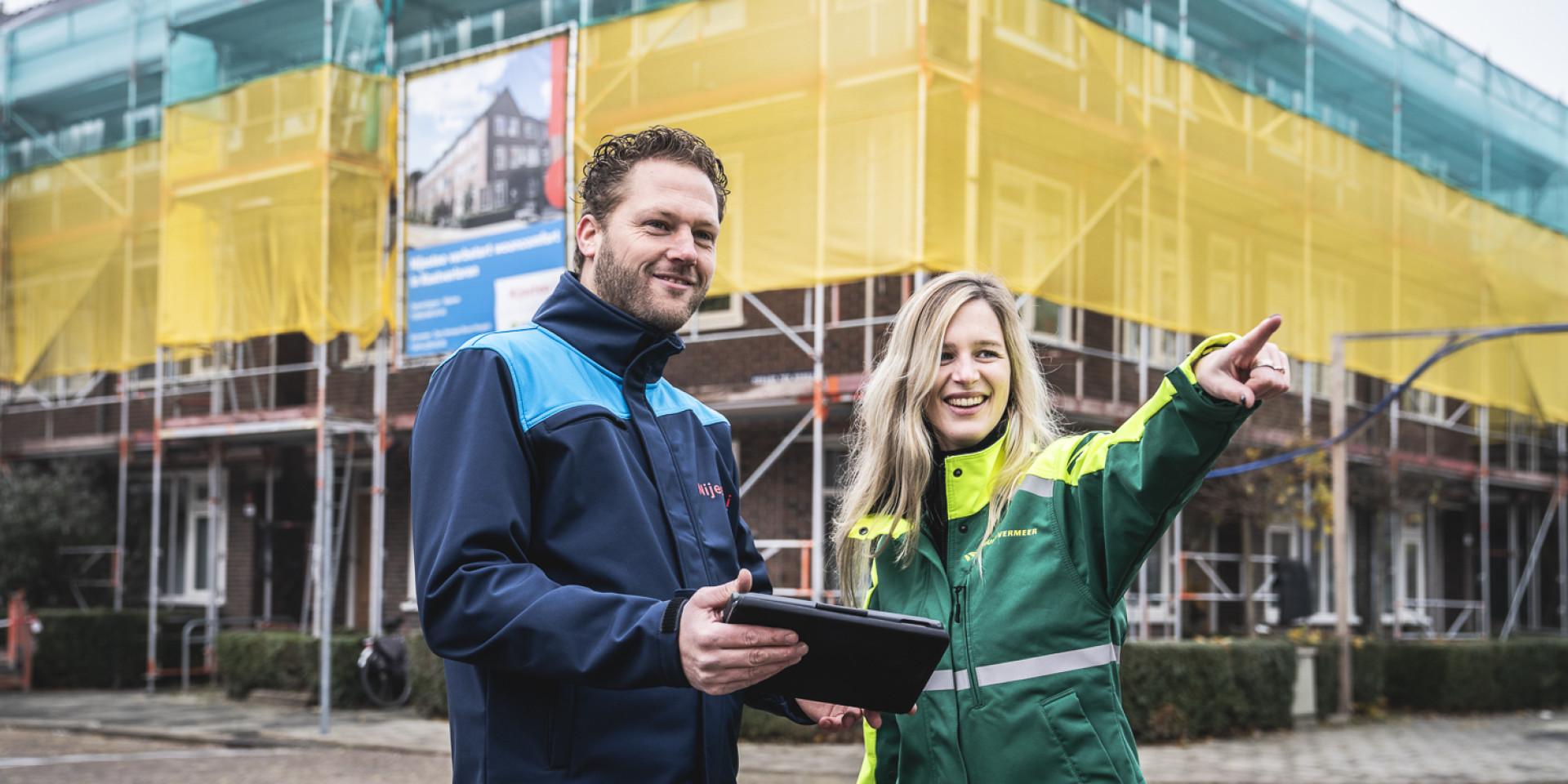Twee mensen staan voor een gebouw in de steigers en bespreken een project.